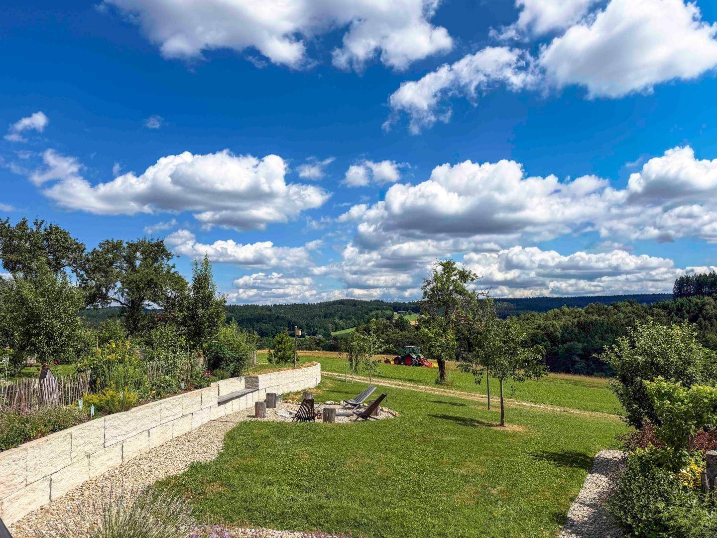 Entspannter Gartenbereich mit Feuerstelle, Liegestühlen und weitem Blick auf die grüne Landschaft.