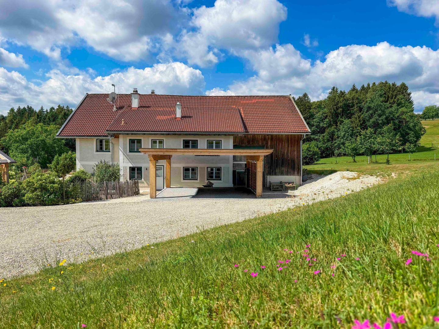 Landhaus mit Carport und weitläufiger Zufahrt in ländlicher Umgebung unter blauem Himmel.