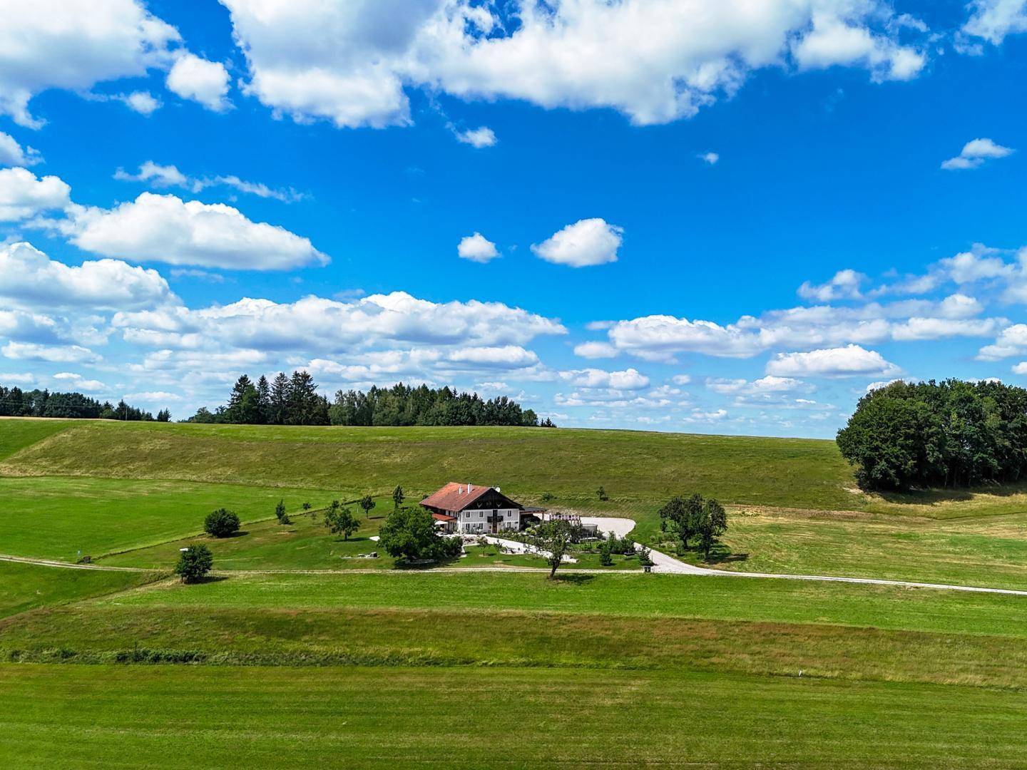 Idyllisches Landhaus eingebettet in eine sanfte Hügellandschaft mit weiten Feldern und Wald.