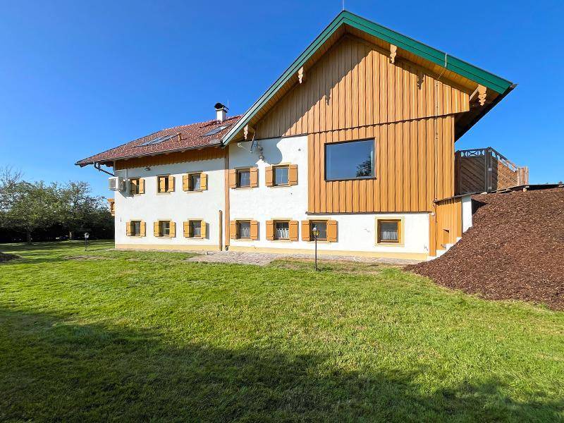Rückansicht des Hauses mit Holzfassade, großen Fenstern und weitläufiger Rasenfläche.