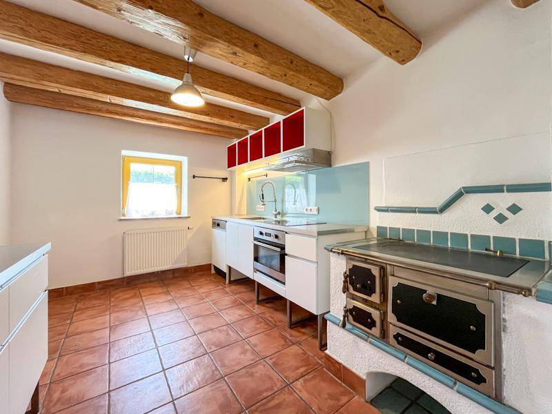 Rustikale Küche mit Terrakotta-Fliesenboden, sichtbaren Holzbalken und traditionellem Kachelofen.