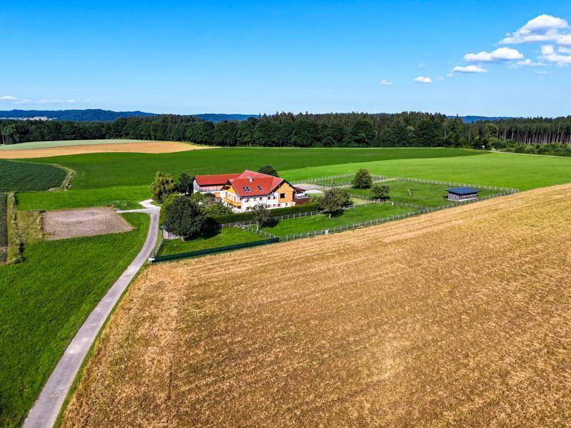 Weitläufiges Anwesen mit Gebäuden, umgeben von grünen Feldern und Wäldern unter blauem Himmel.