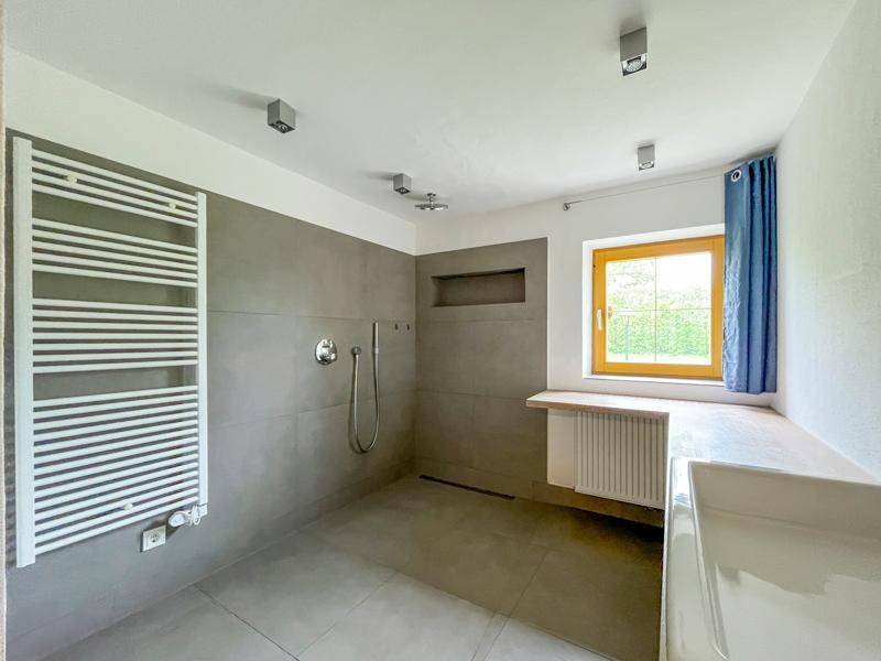 Modernes Badezimmer mit grauen Fliesen, großer begehbarer Dusche und beheiztem Handtuchhalter.