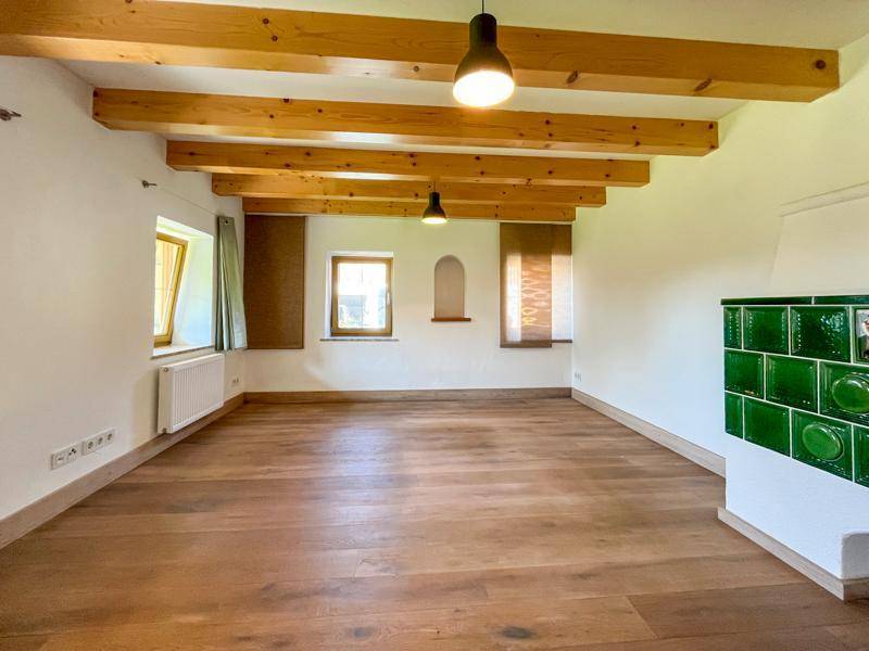 Geräumiger Wohnbereich mit sichtbaren Holzbalken an der Decke und hellem Parkettboden.