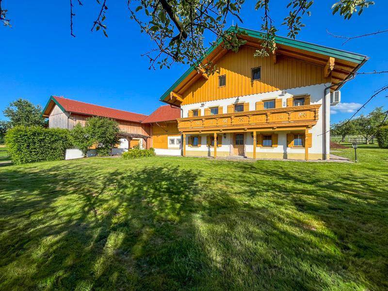 Charmantes Landhaus mit traditioneller Holzverkleidung und Balkonen, eingebettet in eine grüne Landschaft.
