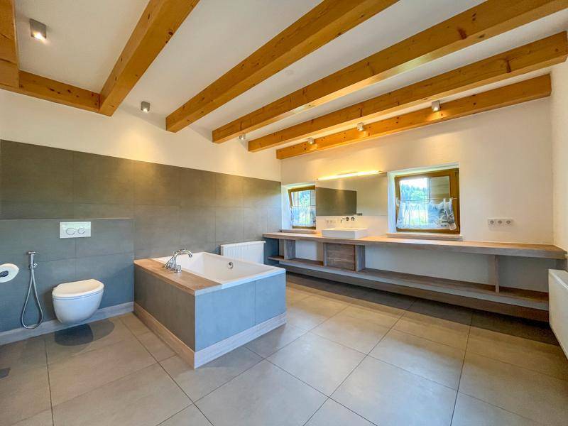 Großes Badezimmer mit freistehender Badewanne, Doppelwaschbecken und sichtbaren Holzbalken.