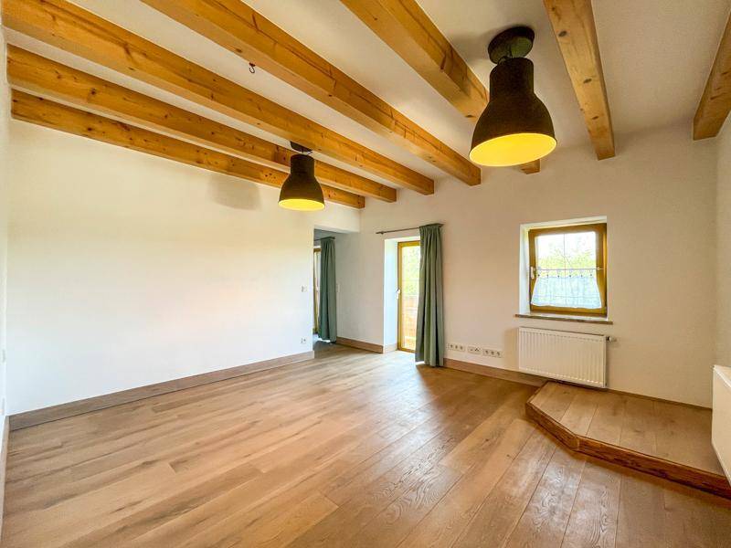 Geräumiger, heller Raum mit Holzbalken an der Decke und hochwertigem Parkettboden.