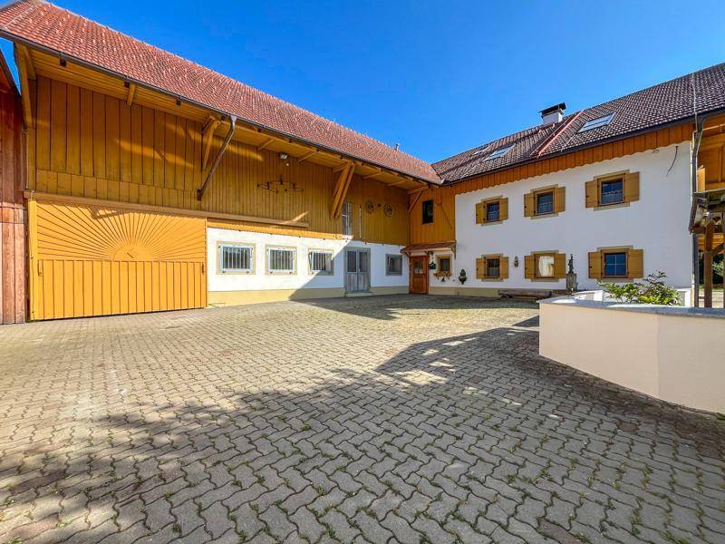 Gepflasterter Innenhof zwischen dem Wohnhaus und einem großen Scheunengebäude mit Holztoren.