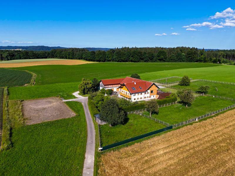 Luftaufnahme eines Anwesens mit mehreren Gebäuden, umgeben von weiten Feldern und Wäldern.