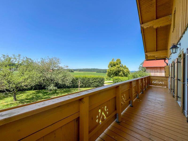 Langer Holzbalkon mit traditionellem Geländer und weitem Blick über grüne Felder und Bäume.