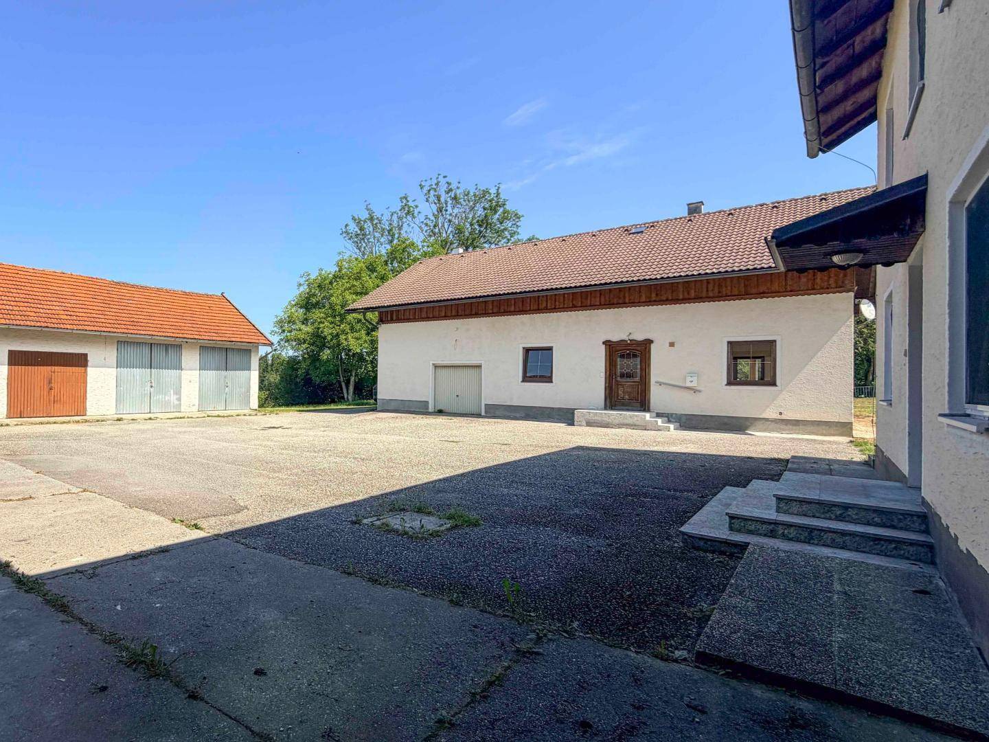 Ländliches Anwesen mit großem gepflastertem Hof und Nebengebäuden unter blauem Himmel.
