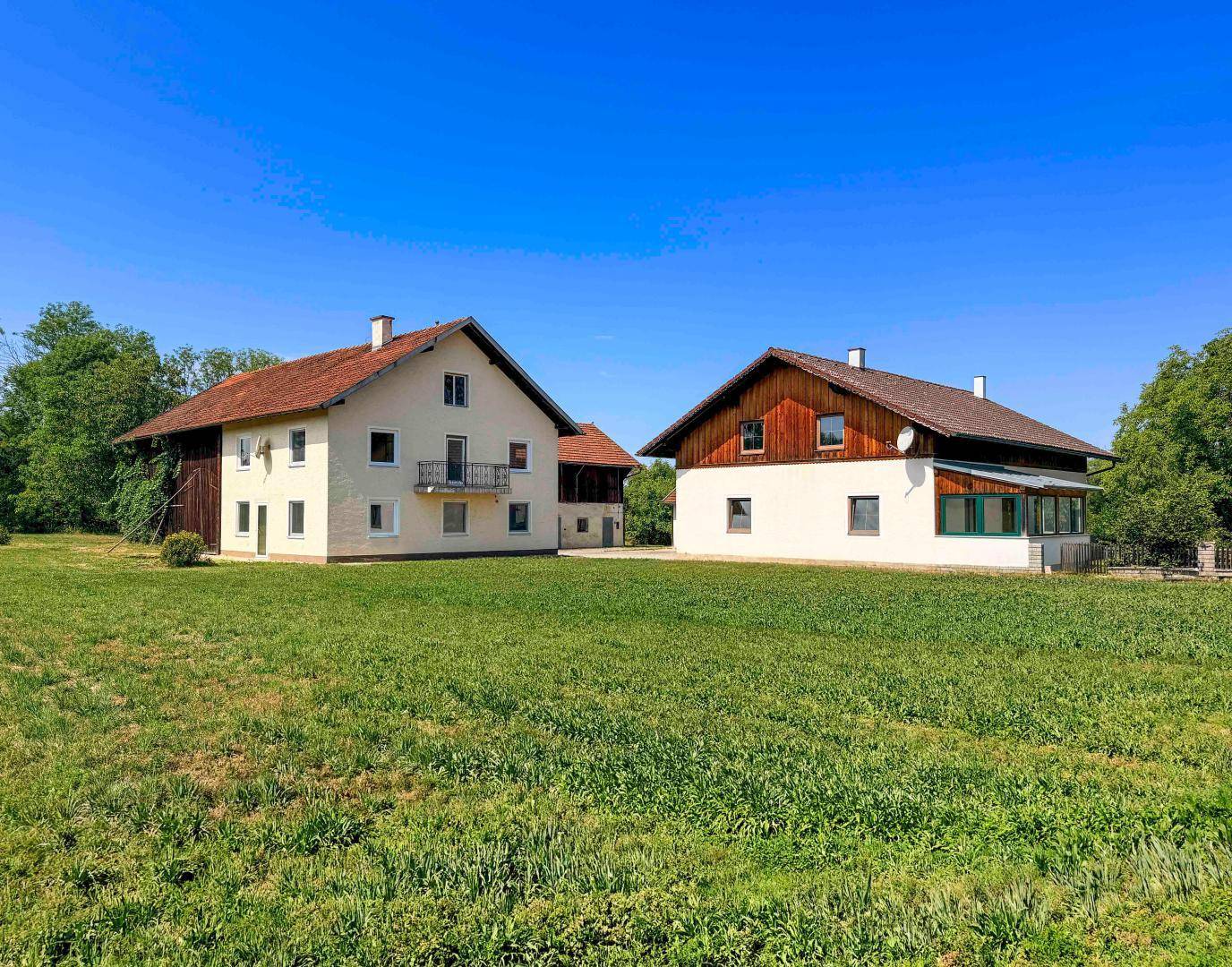 Zwei traditionelle Häuser mit roten Ziegeldächern und Balkon in ländlicher Umgebung.