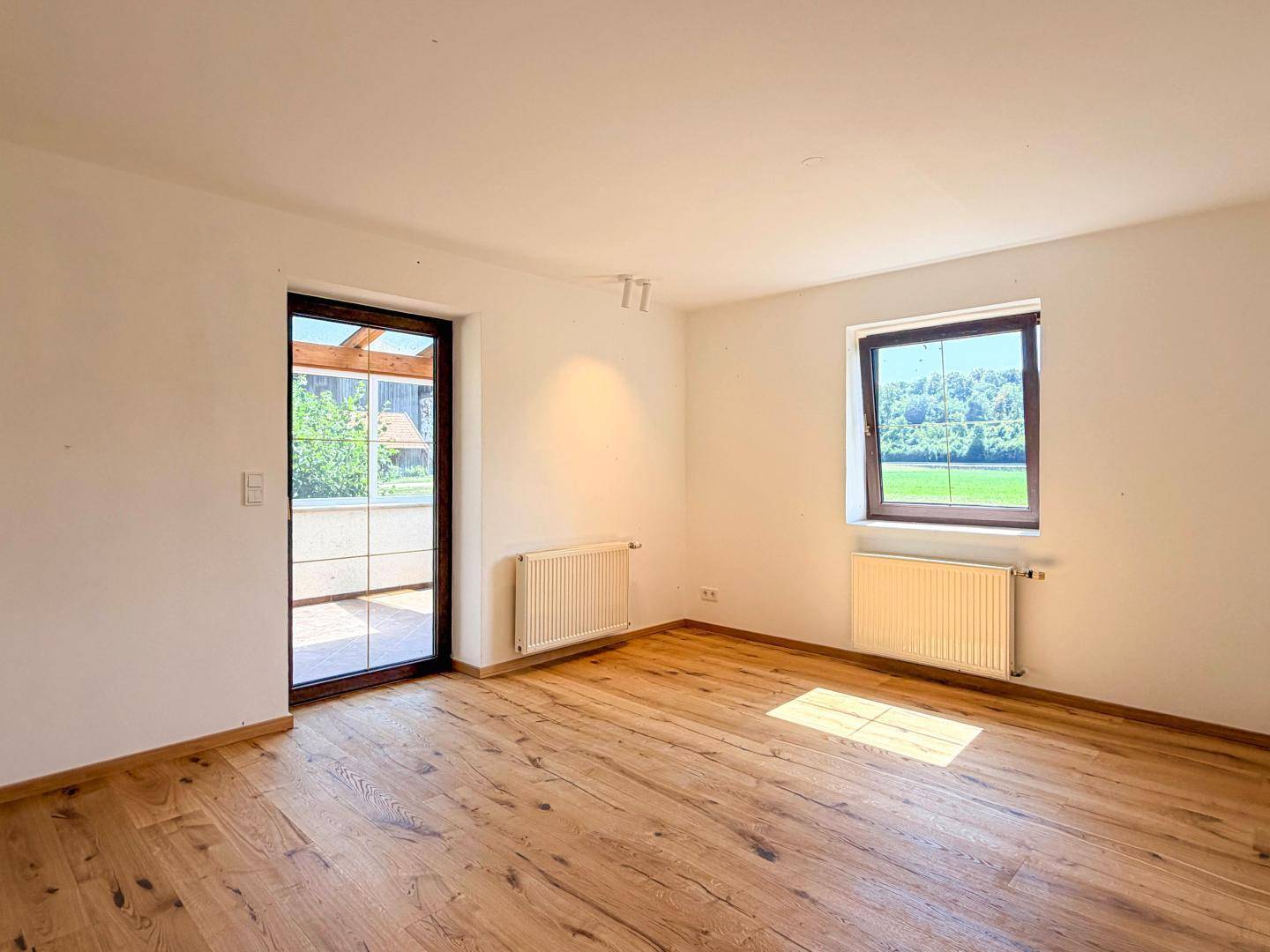 Heller Raum mit Holzboden, Heizkörper und Zugang zu einem Außenbereich.