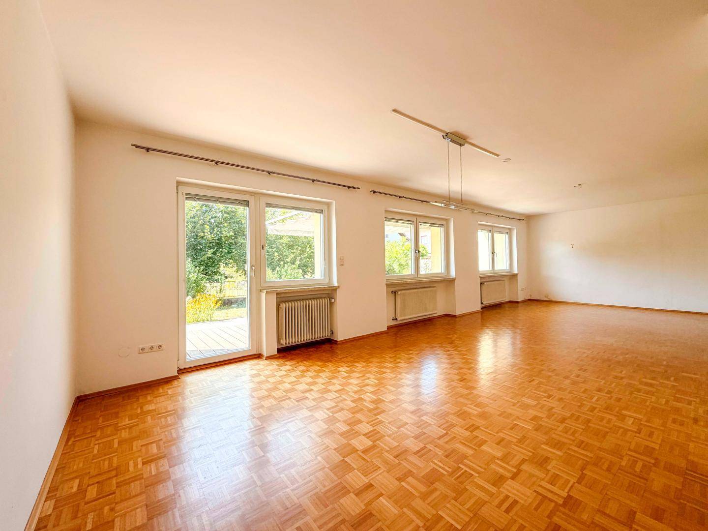 Geräumiges Wohnzimmer mit Parkettboden und großen Fenstern zum Garten.