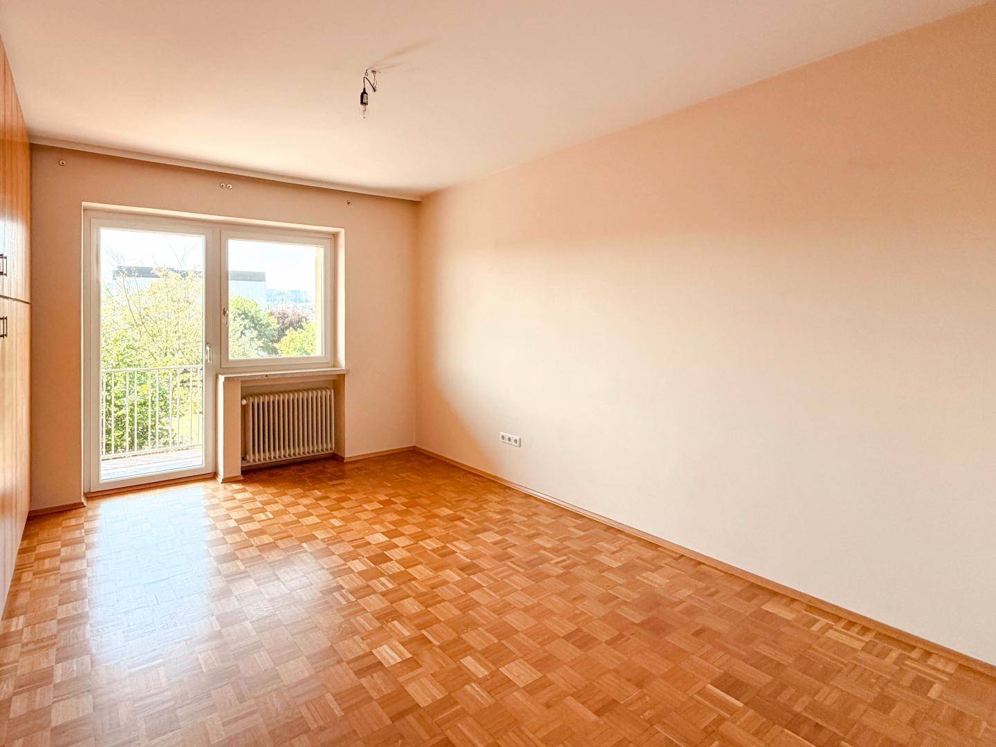 Schlafzimmer mit Parkettboden, großem Fenster und Zugang zu einem Balkon.