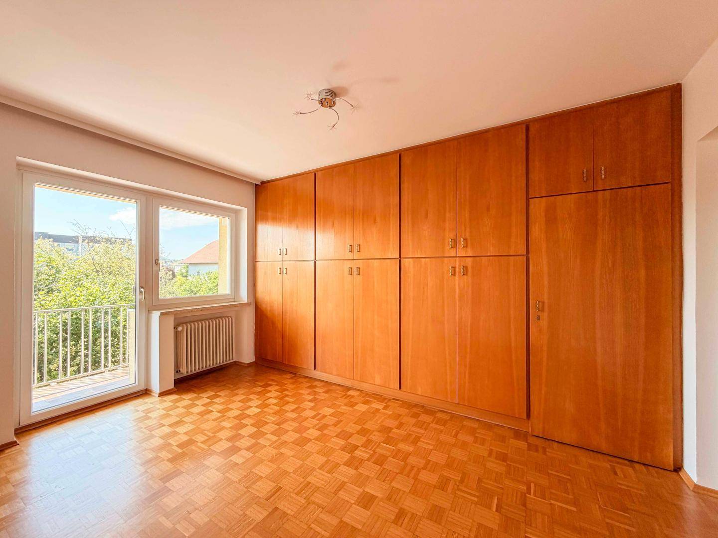 Schlafzimmer mit Parkettboden und einer langen Reihe von Einbauschränken aus Holz.