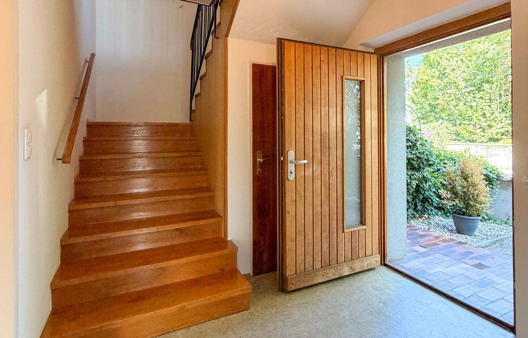 Heller Eingangsbereich mit Holztreppe und offener Haustür zum Außenbereich.