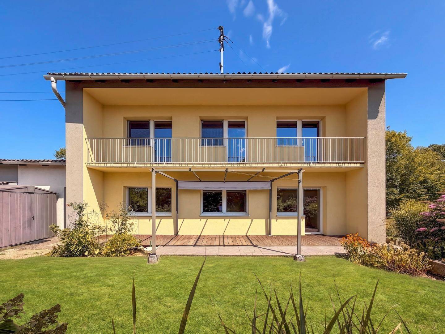 Vollansicht der Hausfassade mit Balkon, Holzterrasse und weitläufigem Garten.