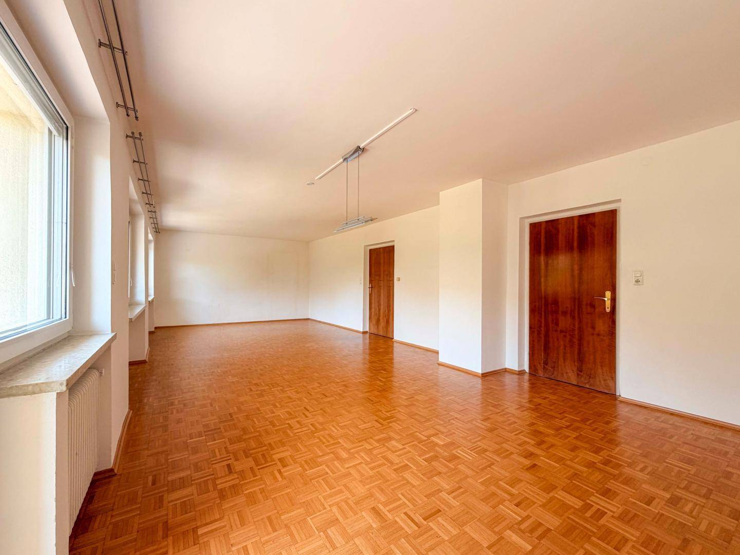 Weitläufiges Wohnzimmer mit Parkettboden und zwei Holztüren, unmöbliert.