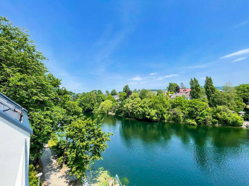 Malerischer Ausblick auf den Fluss und die üppige grüne Uferlandschaft unter blauem Himmel.