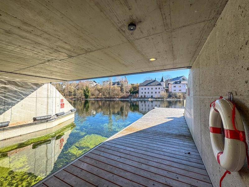 Überdachter Bootsanlegeplatz mit Holzsteg und Blick auf die gegenüberliegende Uferbebauung.