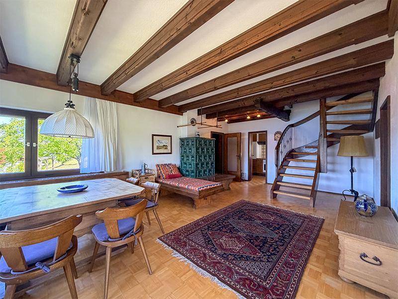 Geräumiger Wohn-Essbereich mit Kachelofen, Holztreppe und traditionellem Interieur unter Holzbalken.