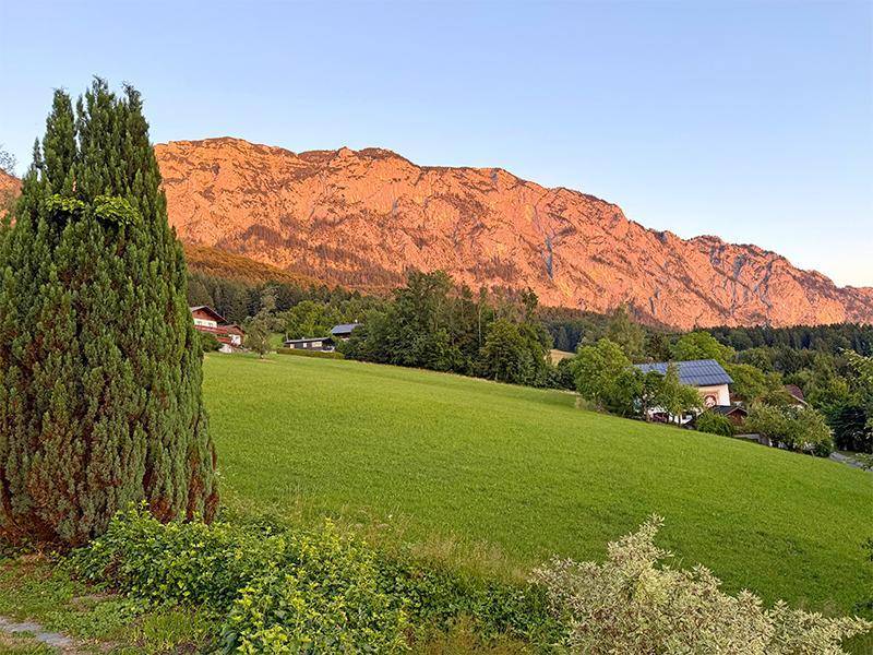 Malerische Landschaft mit grünen Wiesen und sonnenbeschienenen Bergen am Abendhimmel.