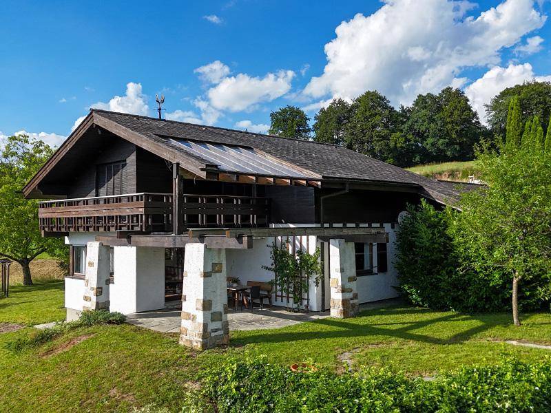 Traditionelles Haus mit Holzbalkonen und überdachter Terrasse, eingebettet in eine grüne Hügellandschaft.