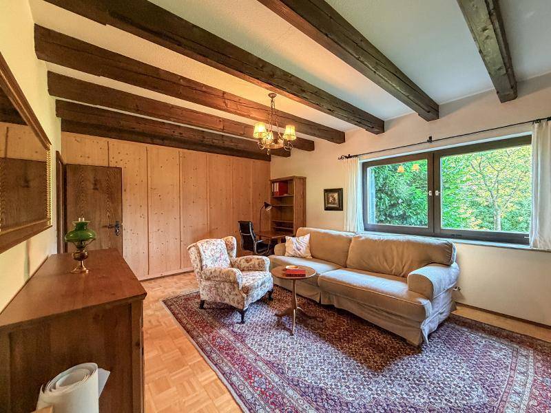 Gemütliches Schlafzimmer mit Holzwänden, Sofa und Blick ins Grüne unter sichtbaren Holzbalken.