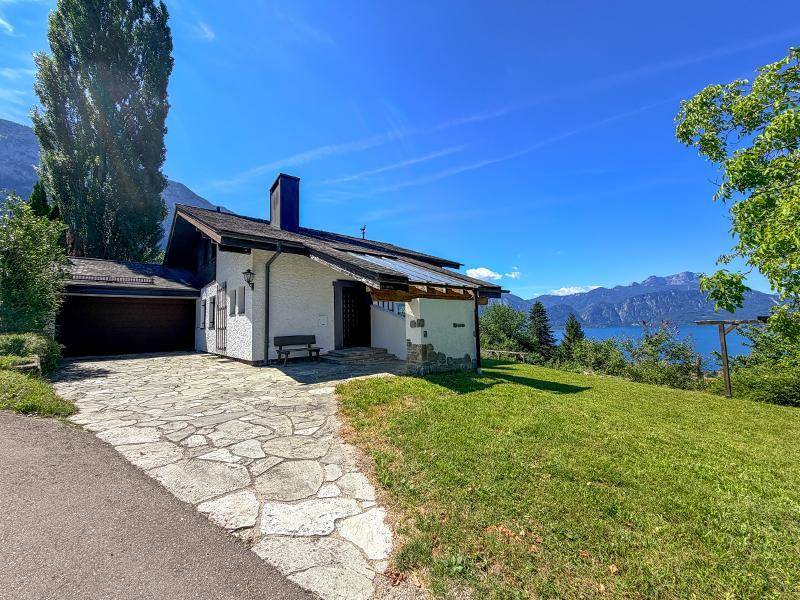 Hausfassade mit gepflastertem Zugang, Garage und weitem Blick auf den See und die Berge.