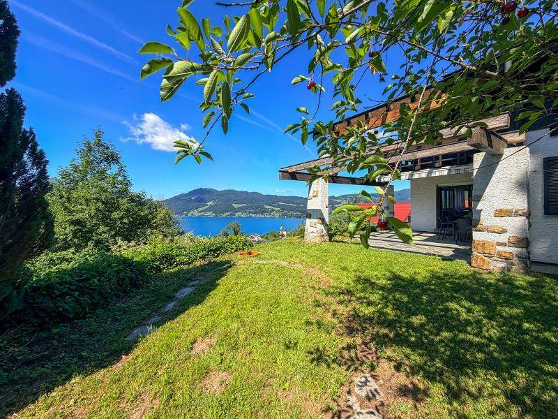 Grüne Rasenfläche neben dem Haus mit überdachter Terrasse und malerischem Seeblick.