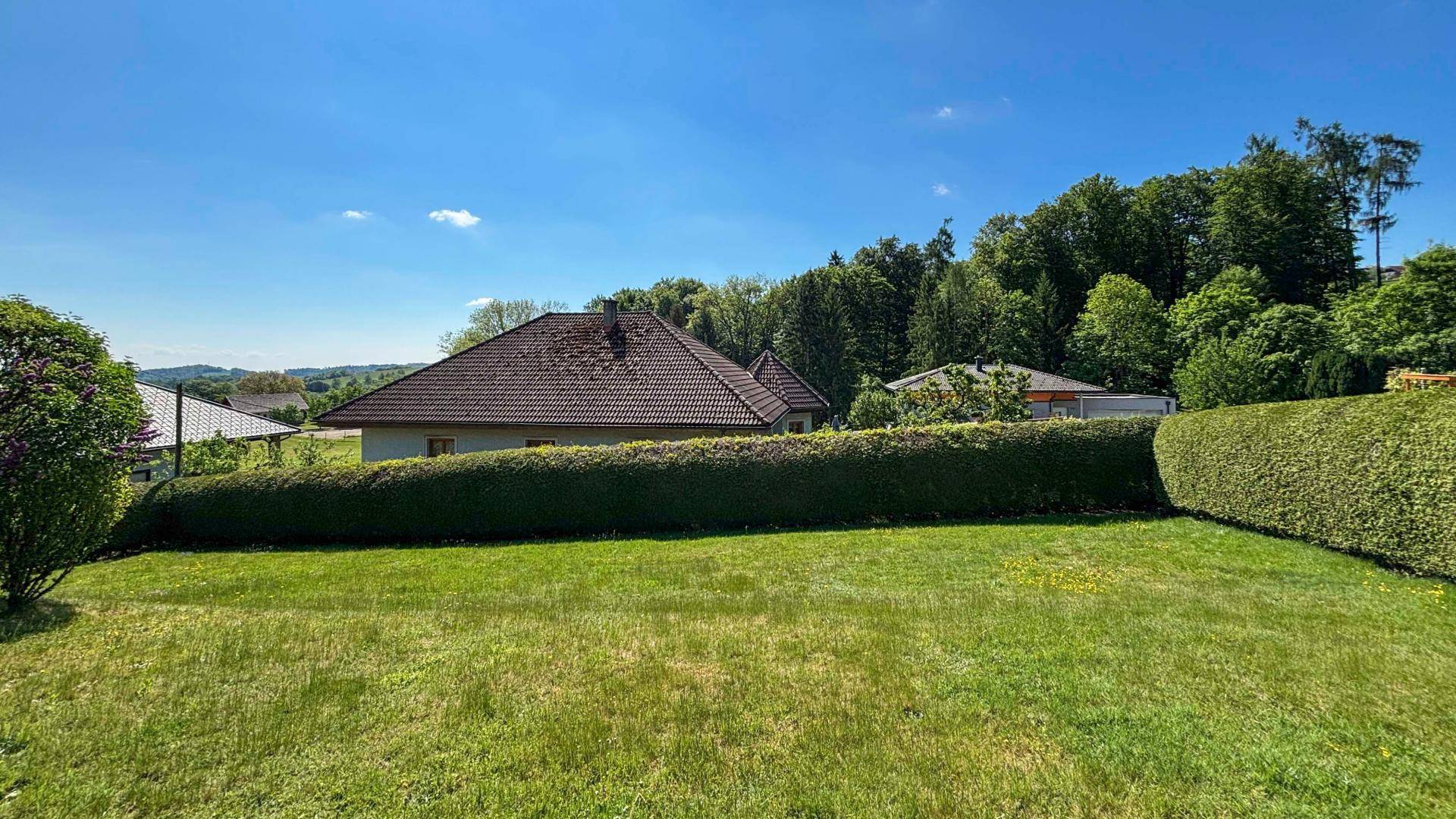 Weitläufiger Gartenbereich mit gepflegtem Rasen, hohen Hecken und Blick auf bewaldete Hügel.