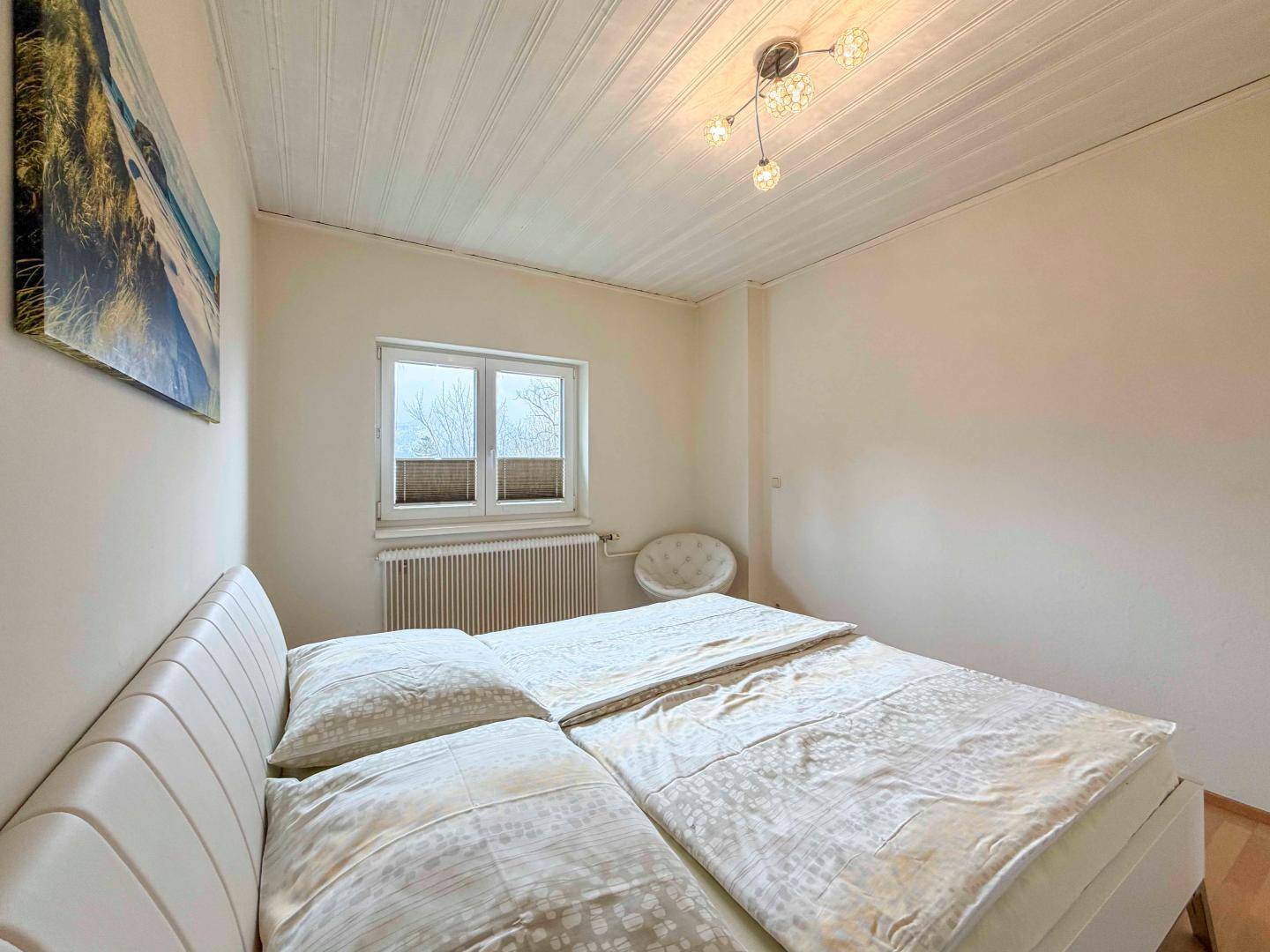 Gemütliches Schlafzimmer mit Doppelbett, hellem Holzboden und einer Fensterfront.
