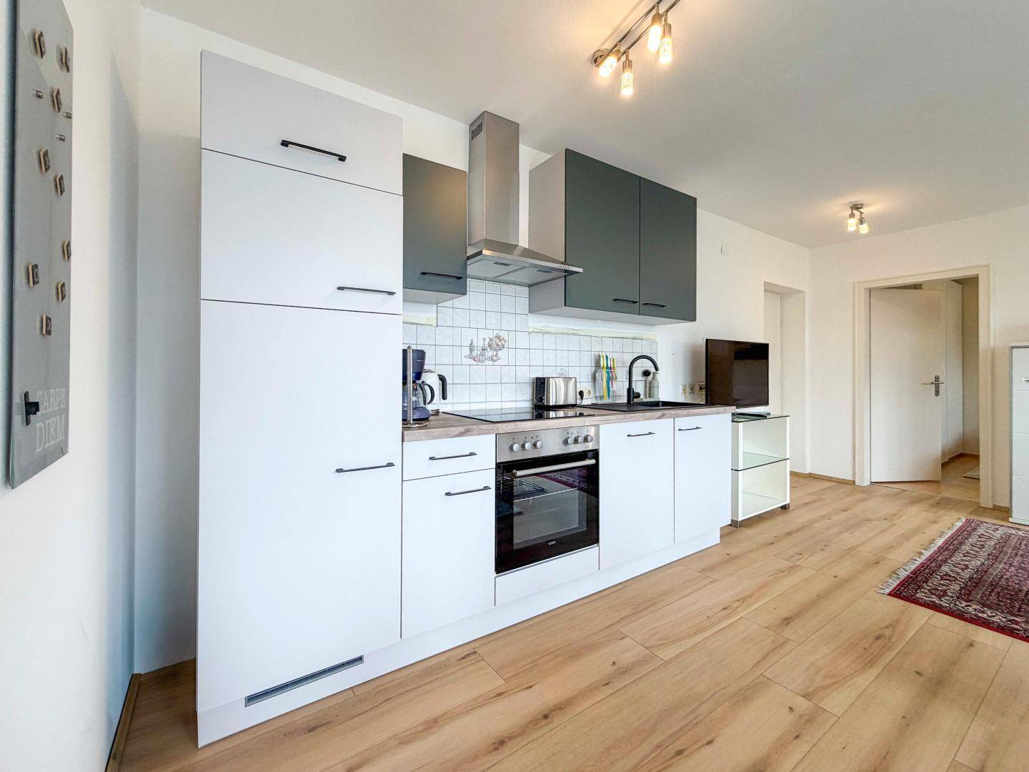 Moderne Einbauküche mit weißen Fronten, integrierten Geräten und Dunstabzugshaube.