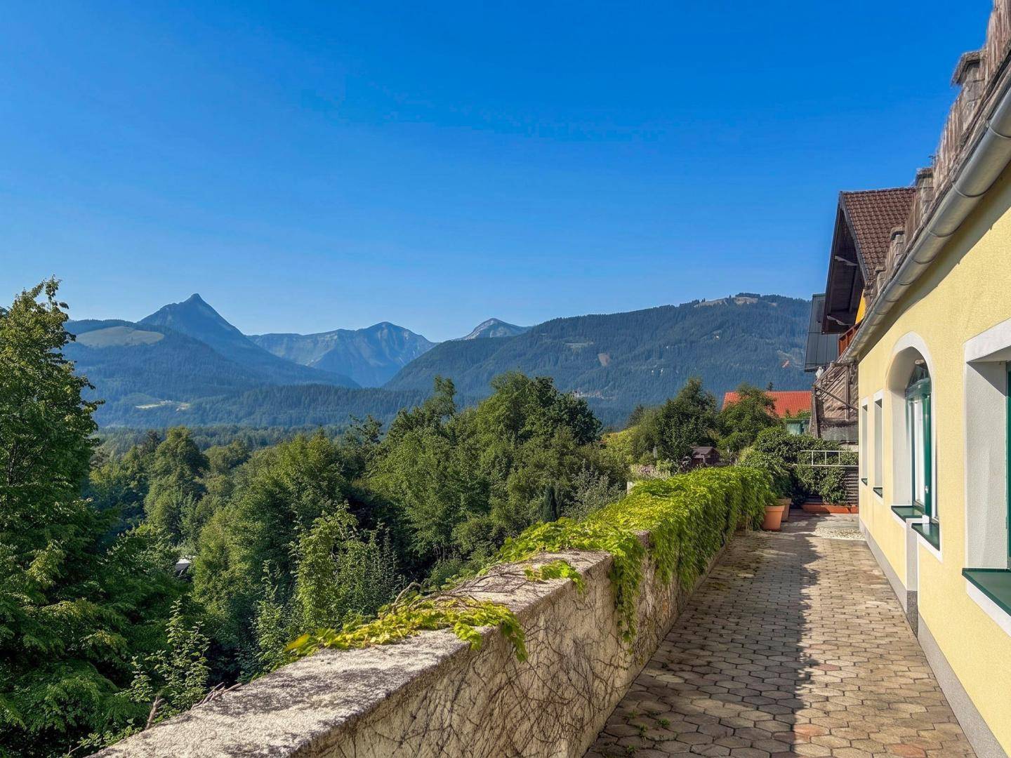 Malerischer Weg entlang des Hauses mit üppiger Bepflanzung und weitem Blick auf die Berge.