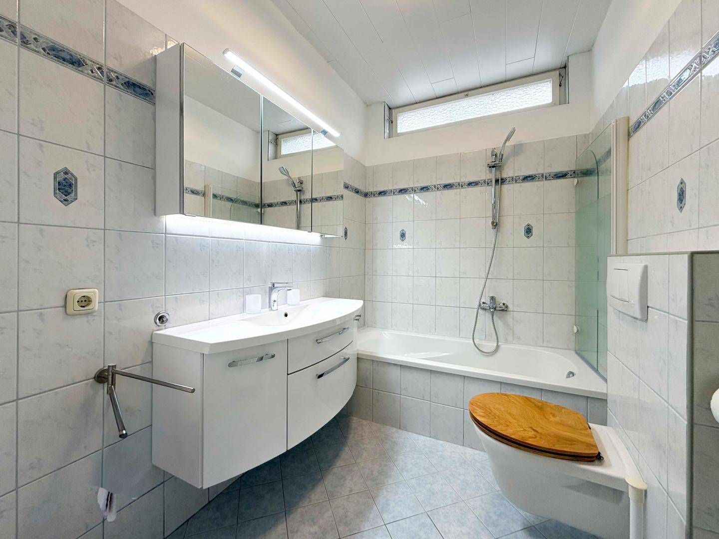 Funktionales Badezimmer mit Badewanne, Duschfunktion, Waschbecken und Spiegelschrank.