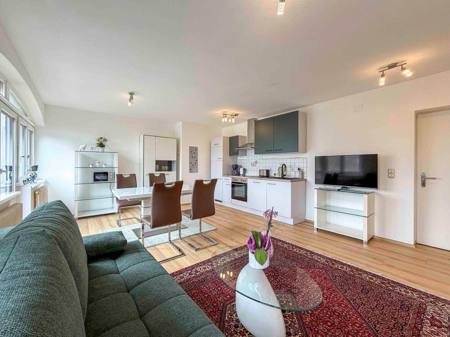 Gemütlicher Wohnbereich mit Sofa, Esstisch und integrierter Küche, alles auf hellem Holzboden.