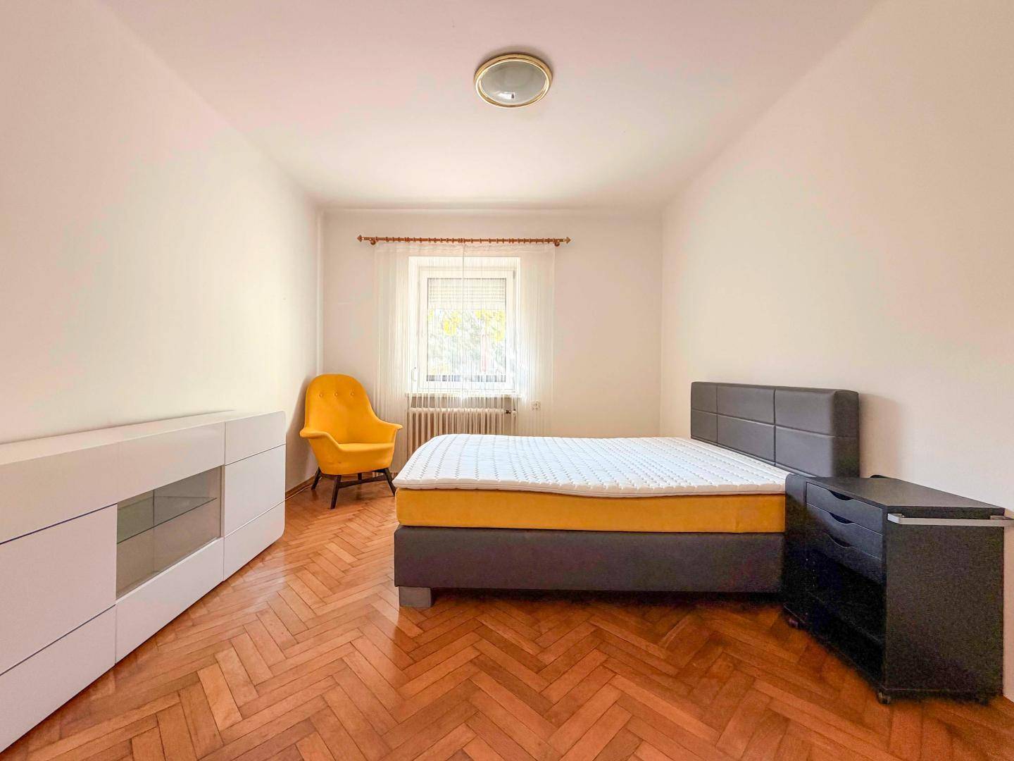 Gemütliches Schlafzimmer mit Fischgrätparkett, Doppelbett und einem gelben Sessel.