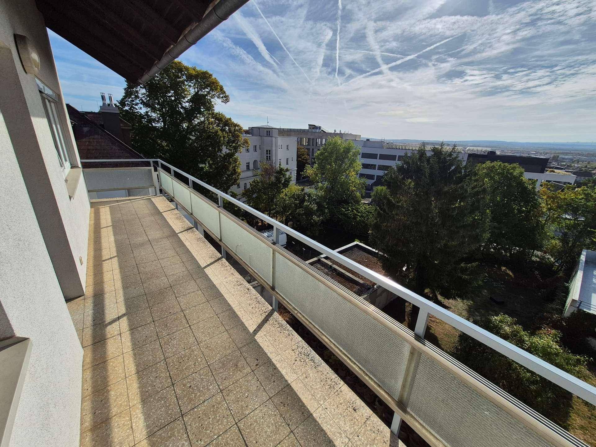 Breiter Balkon mit Fliesenboden und einer weiten Aussicht auf die Stadt und die umliegende Natur.