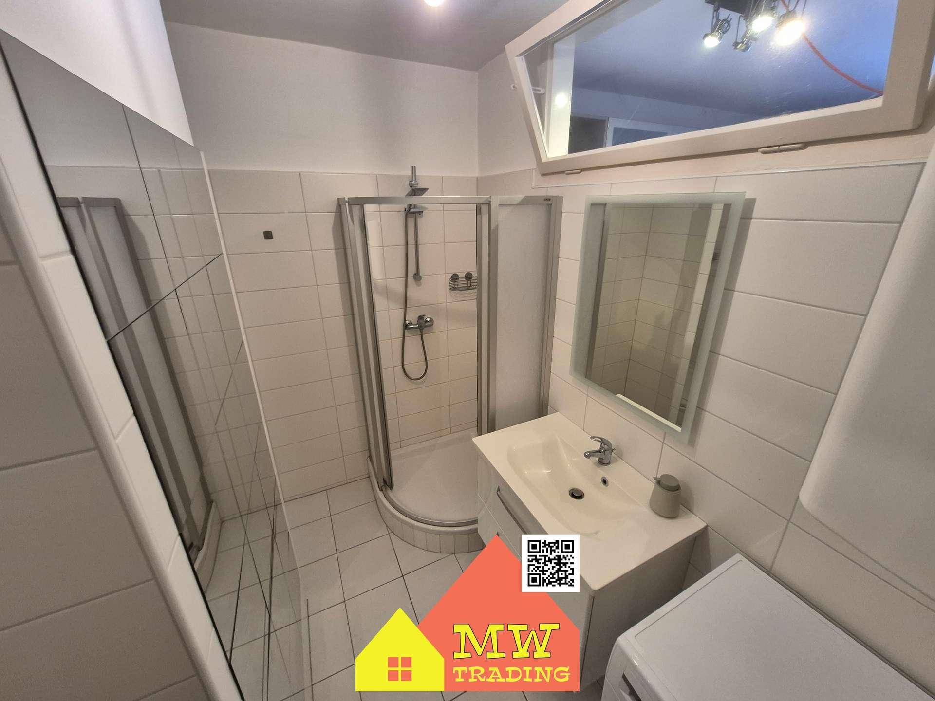 Modernes Badezimmer mit weißen Fliesen, Duschkabine und Waschtischunterschrank.