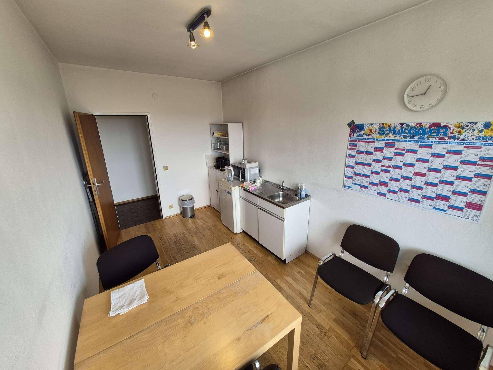 Funktionale Teeküche mit Holzboden, kleiner Küchenzeile und einem Tisch mit Stühlen.