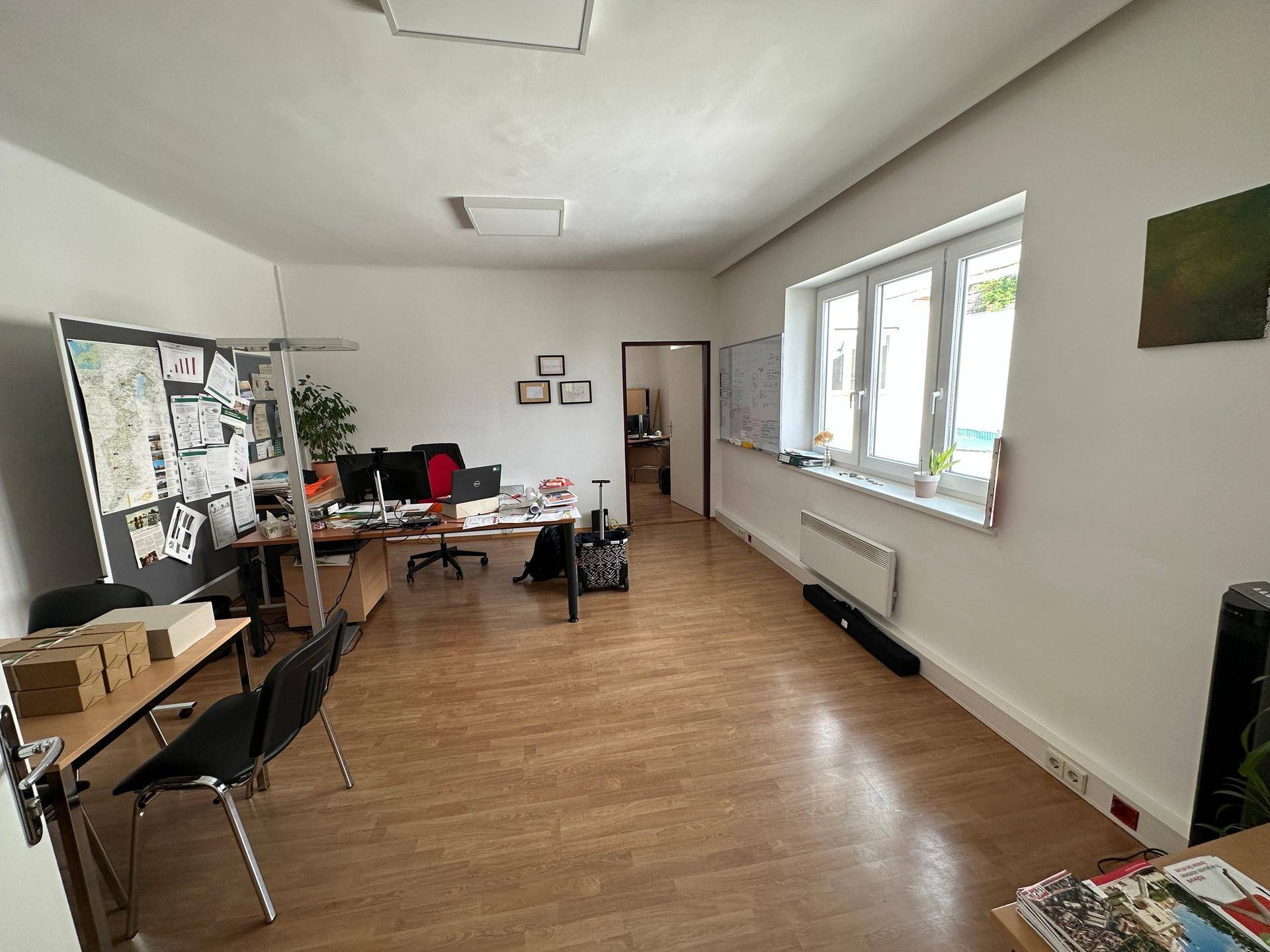 Geräumiges Büro mit Holzfußboden, großen Fenstern und mehreren Arbeitsplätzen, ideal für ein Team.