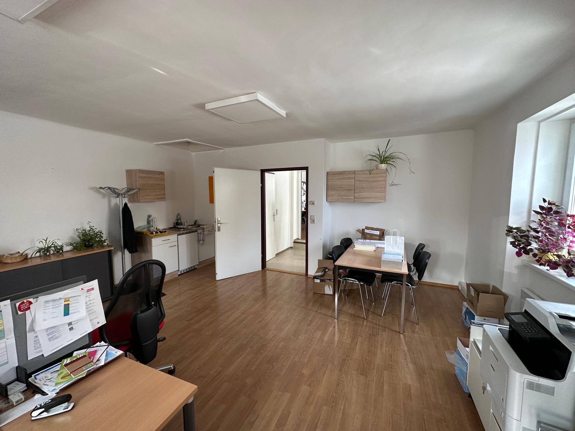Großes Büro mit Holzfußboden, mehreren Arbeitsbereichen und einer kleinen integrierten Küchenzeile.
