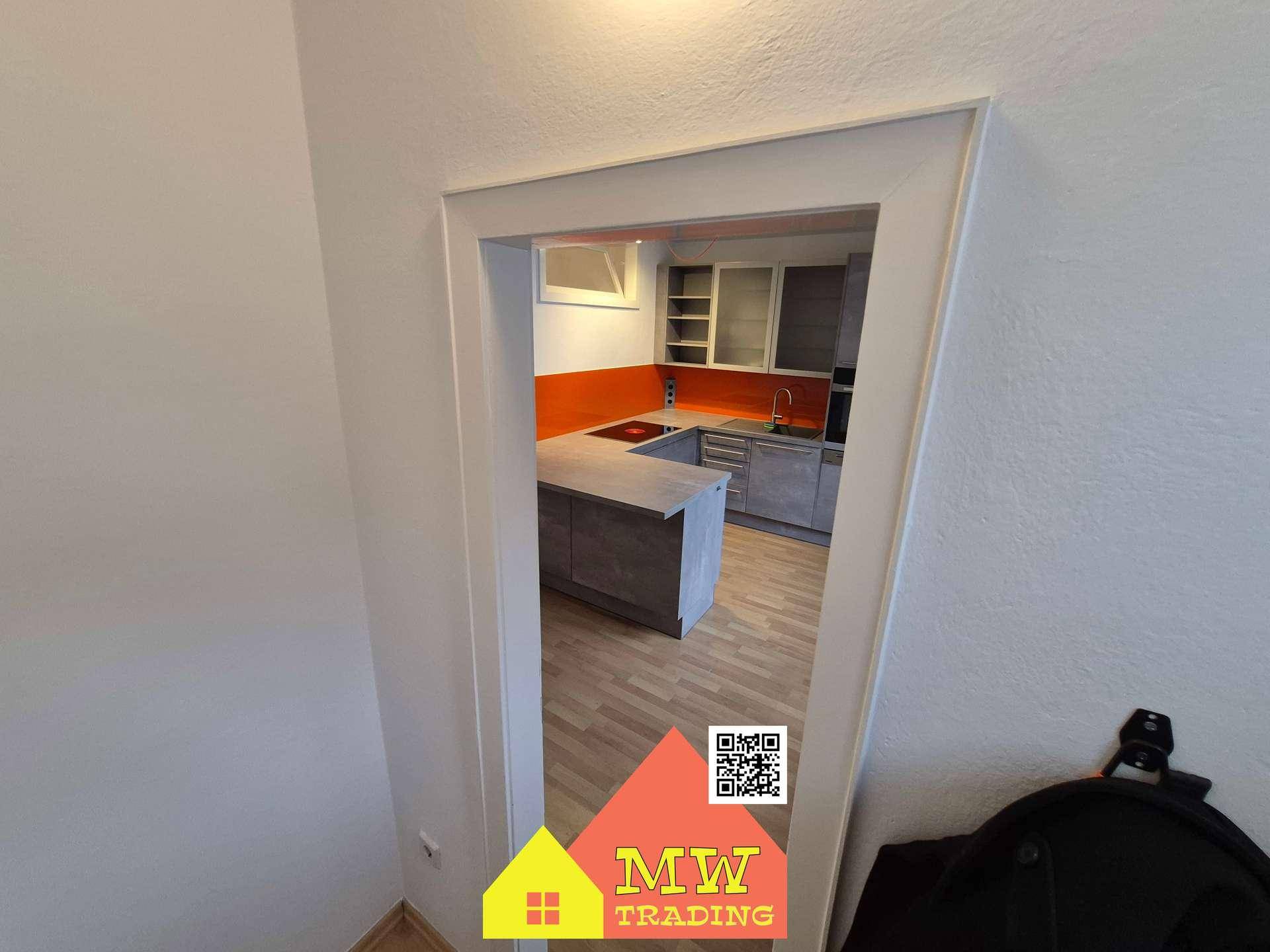 Blick durch eine Tür in die moderne Küche mit grauen Schränken und orangefarbener Rückwand.