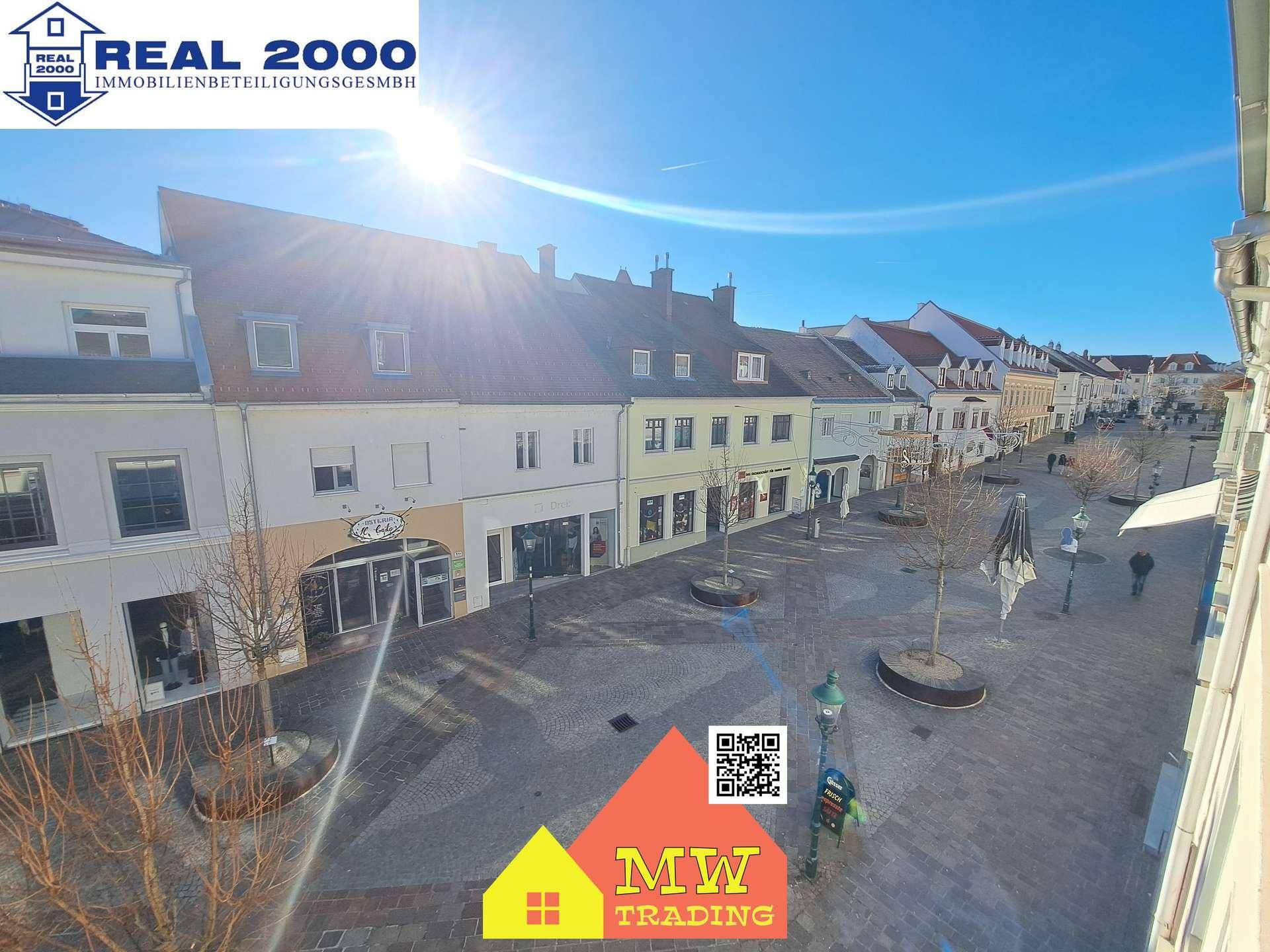 Sonnige Ansicht einer belebten Einkaufsstraße mit historischen Gebäuden und blauem Himmel.