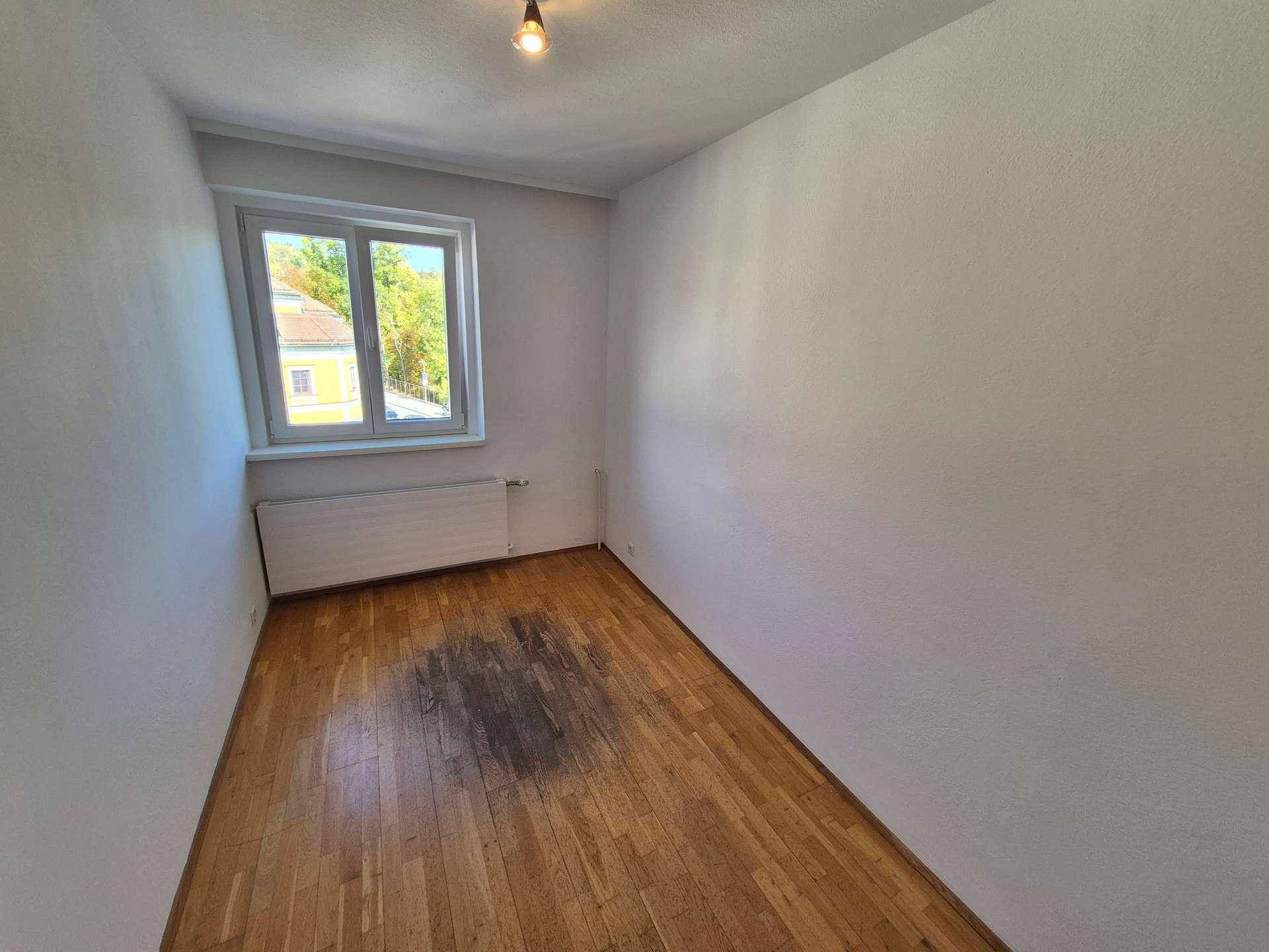 Helles Schlafzimmer mit Holzboden und einem Fenster, das einen Ausblick auf die Umgebung bietet.