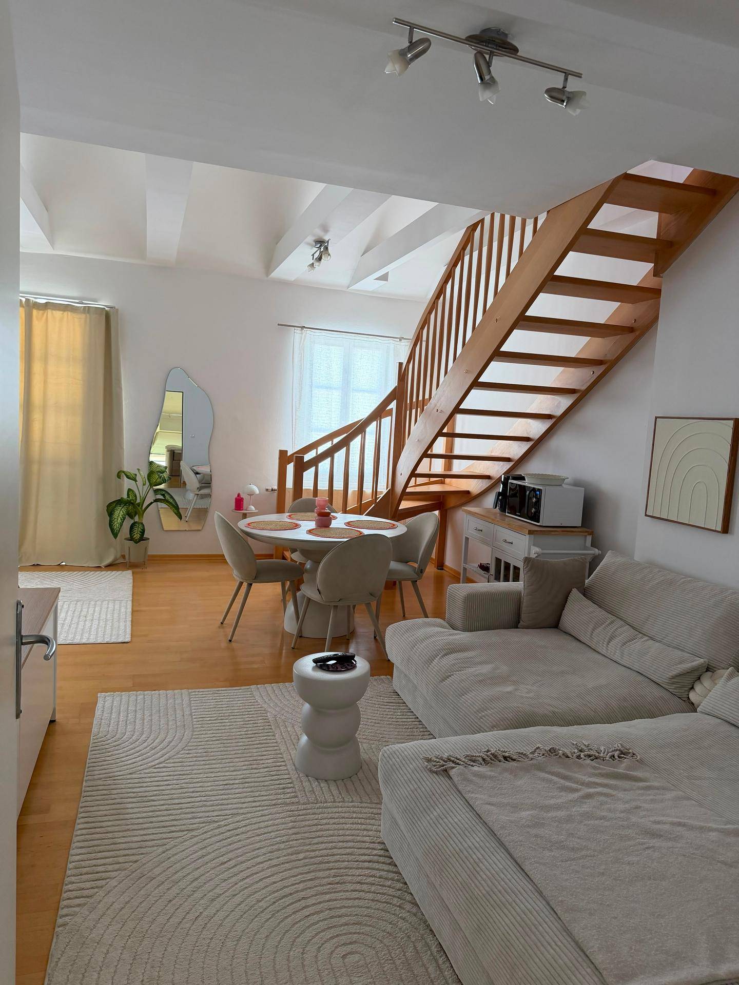 Gemütlicher Wohnbereich mit beigem Sofa, Esstisch und Holztreppe in einem offenen Raumkonzept.