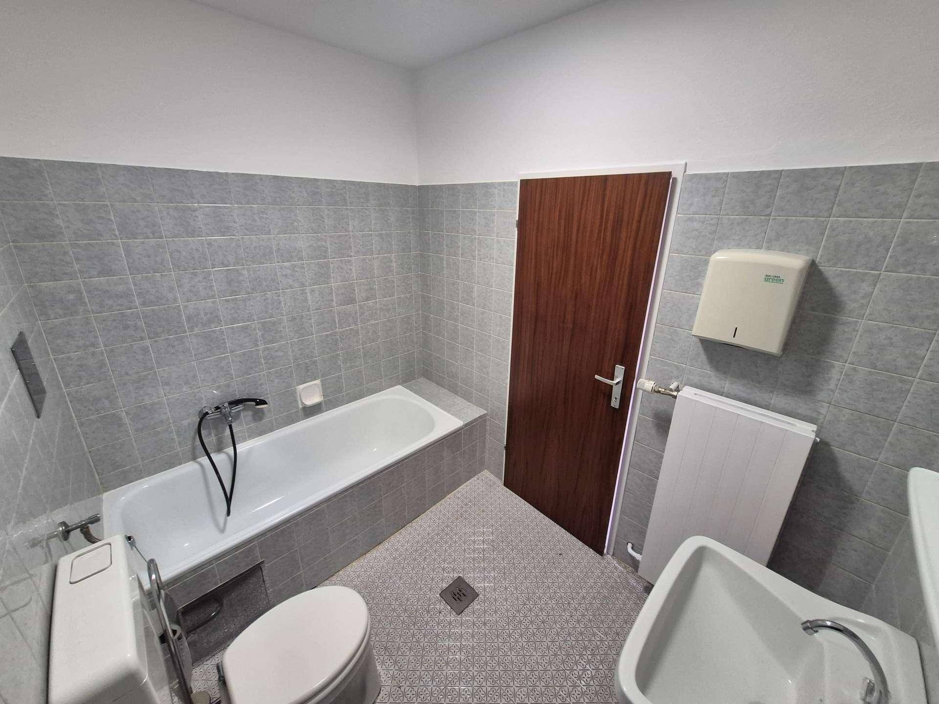 Badezimmer mit grauen Fliesen, Badewanne, Toilette und Heizkörper, in gutem Zustand.