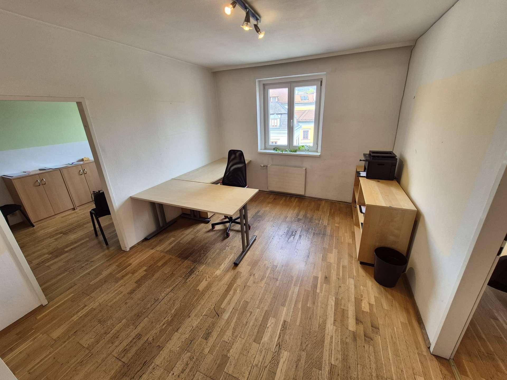 Geräumiges Büro mit Holzboden, zwei Schreibtischen und einem Fenster für Tageslicht.