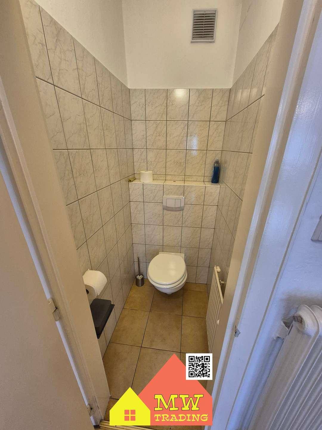 Kleines Gäste-WC mit Wand-WC und hellen Fliesen an Wänden und Boden.